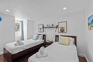 A hotel room with two single beds, a small table, and a nightstand.