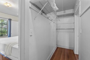 Ein Zimmer mit Holzboden, einem Bett, einem Vorhangfenster und einer Deckenleuchte.