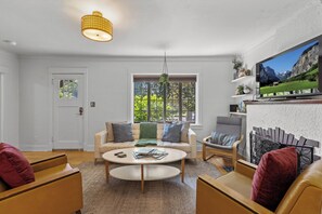 A living room with a sofa, armchairs, a coffee table, a TV mounted on the wall, and a window with a view of greenery. - Boise-Westend-hot tub-Central location 4 bedrooms (Boise)