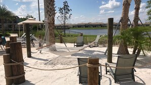 Een strandgedeelte met een hangmat, stoelen en uitzicht op een gebouw aan de overkant van het water.