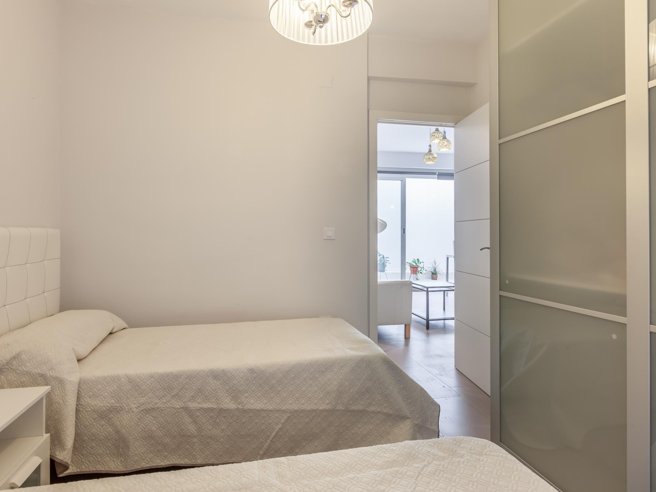 Een slaapkamer met twee bedden, een garderobe en uitzicht op een balkon met planten.