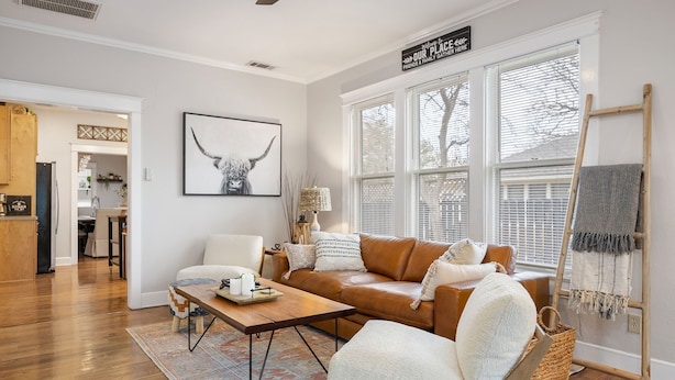A living room with a brown leather sofa, a white armchair, a wooden coffee table, and a large window with blinds. - 4 min walk to Town Square! 3bd 2bath cozy Historical home (Georgetown)