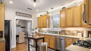 A modern kitchen with wooden cabinets, a stainless steel dishwasher, and a gas stove. - 4 min walk to Town Square! 3bd 2bath cozy Historical home (Georgetown)