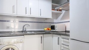 Une cuisine compacte avec des meubles blancs, un lave-linge, un four à micro-ondes et un évier.