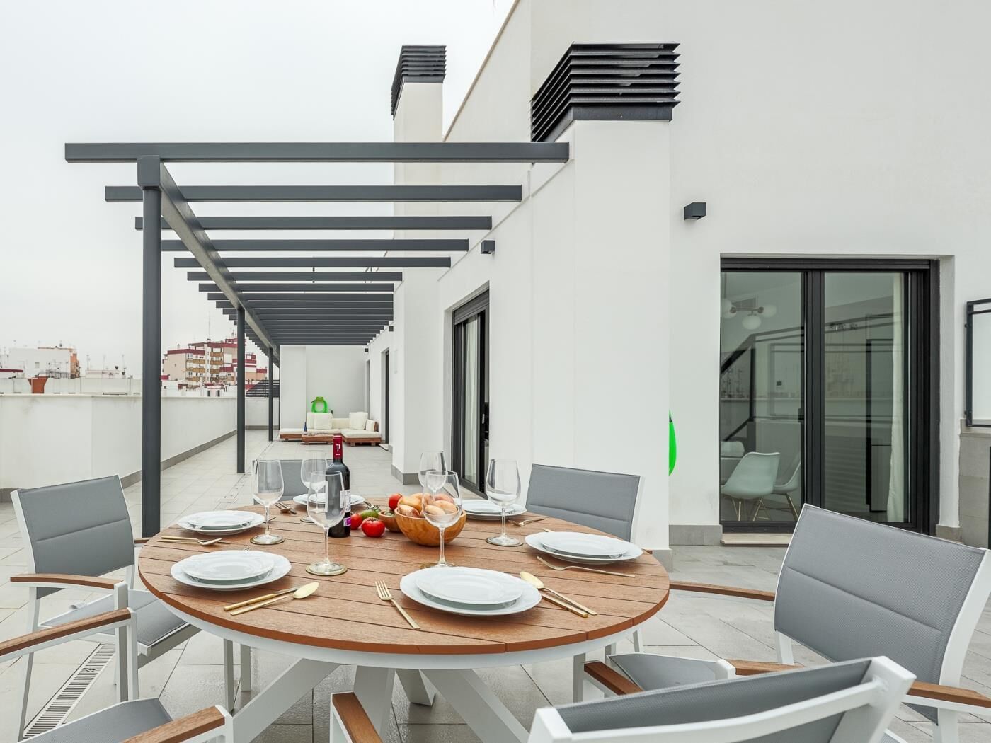 A rooftop terrace with a round wooden table set for dining, surrounded by modern chairs.