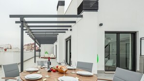 Une terrasse sur le toit, avec une table ronde en bois dressée pour le dîner, entourée de chaises modernes.
