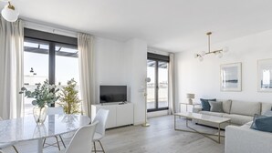 Un salon moderne comprenant un coin repas, un canapé, un téléviseur et une grande fenêtre avec des rideaux.