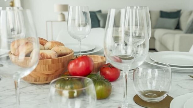 Une table à manger dressée avec du pain, des tomates et des verres à vin.