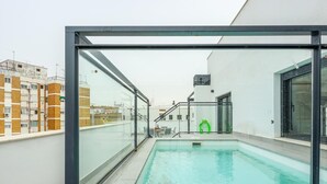 Une piscine sur le toit, dotée de rampes en verre, d’un grand flotteur gonflable vert et offrant une vue sur les bâtiments environnants.