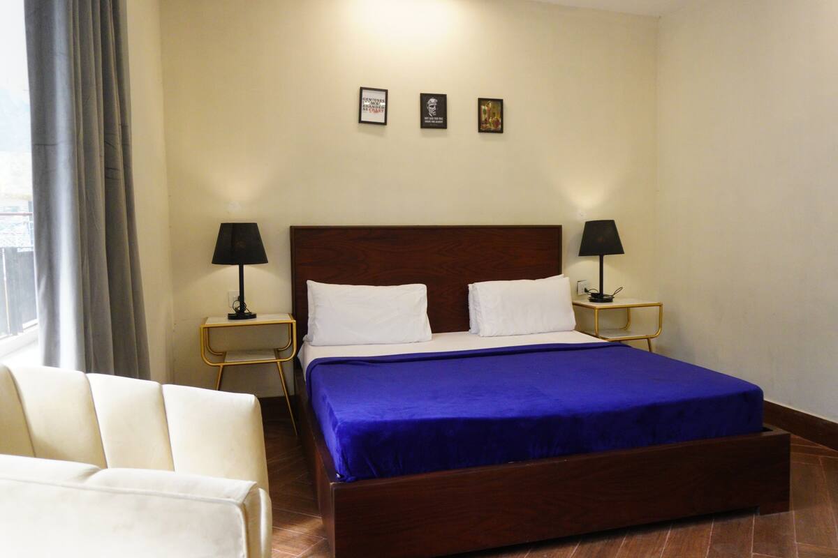 Habitación de hotel con una cama grande, dos mesitas de noche con lámparas, una silla y tres cuadros en la pared.