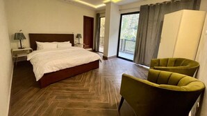A hotel room with a large bed, two bedside tables with lamps, a green armchair, and a view of the outdoors through a balcony. - Point One (Swat)