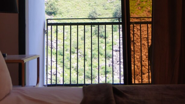 A room with a bed, a nightstand, and a window overlooking a hillside. - Point One (Swat)