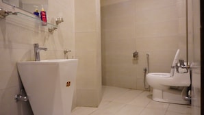 A bathroom with a white sink, a glass shelf with toiletries, a toilet, and a shower area. - Point One (Swat)