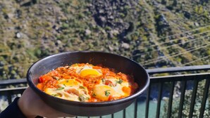 A bowl of shakshuka with eggs, held over a railing with a mountainous landscape in the background. - Point One (Swat)