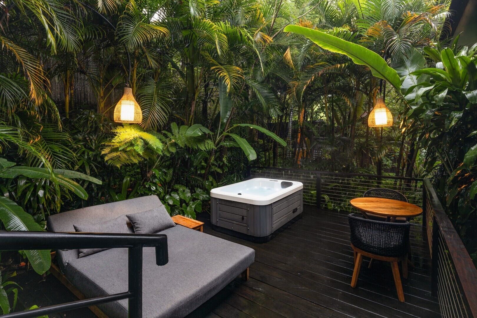 A cozy outdoor seating area with a sofa, a hot tub, and a table, surrounded by lush tropical plants.