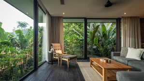 A modern living room with a large window, a sofa, a wooden coffee table, and a chair. - Munduk Cabins by Desa Hay (Munduk)