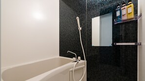 Een moderne badkamer met een wit bad, een handdouche en een spiegel boven een plank met toiletartikelen.