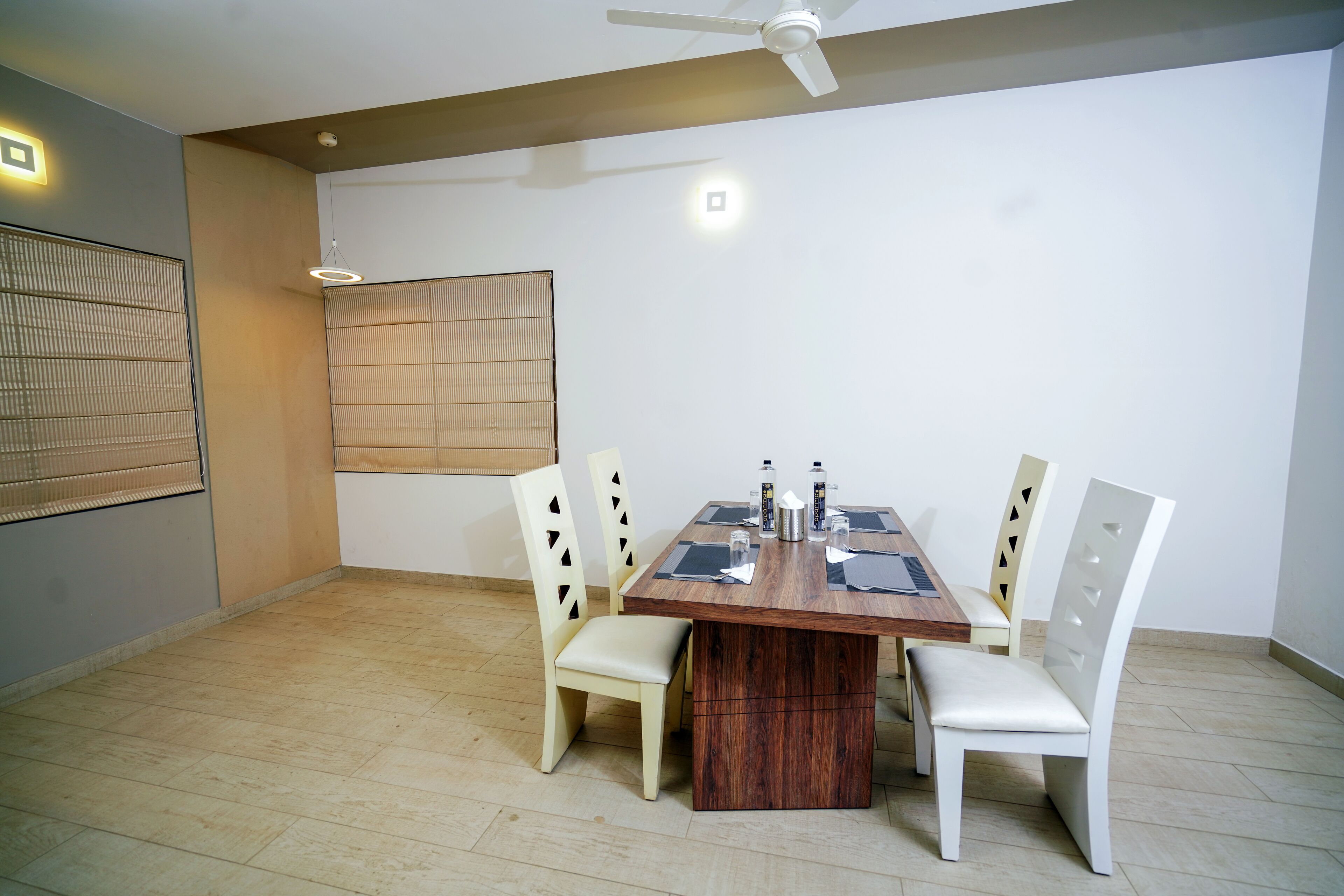 Un comedor con una mesa de madera, cuatro sillas, un ventilador de techo y un ventanal con persianas.