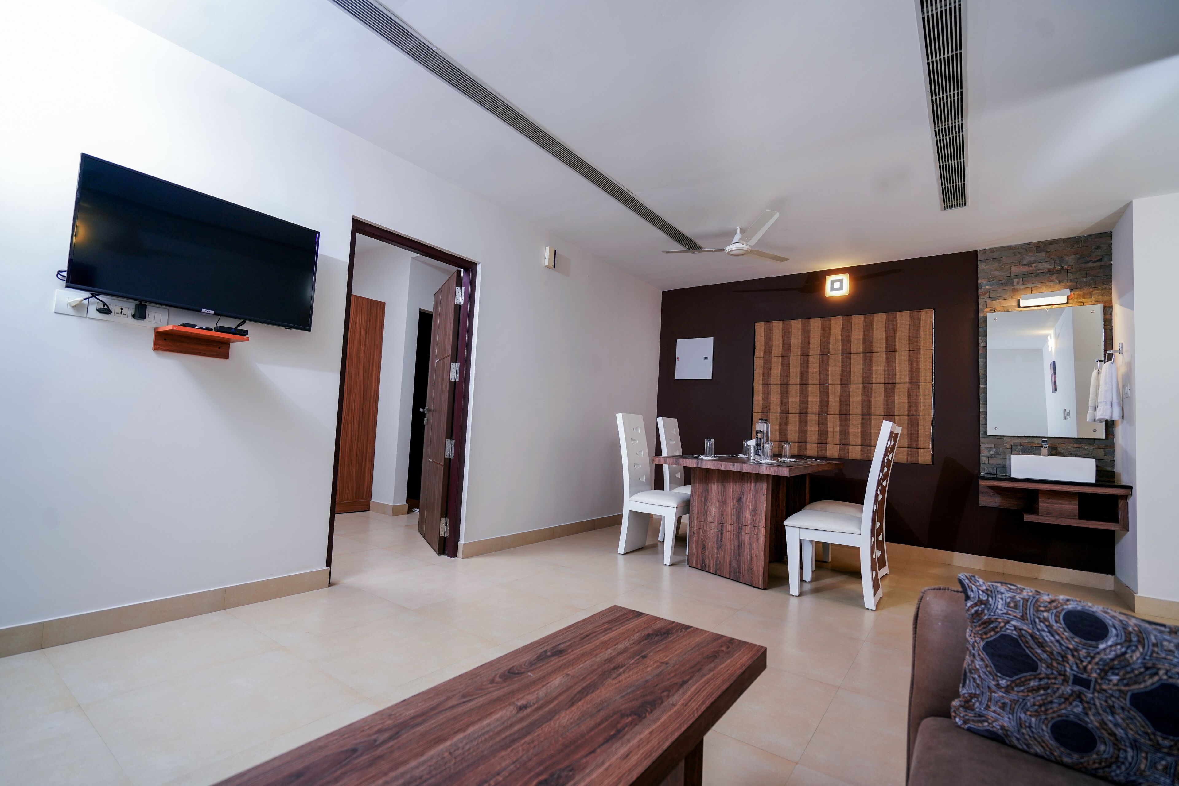 A modern living room with a flat-screen TV, a wooden coffee table, and a brown sofa with a patterned cushion.