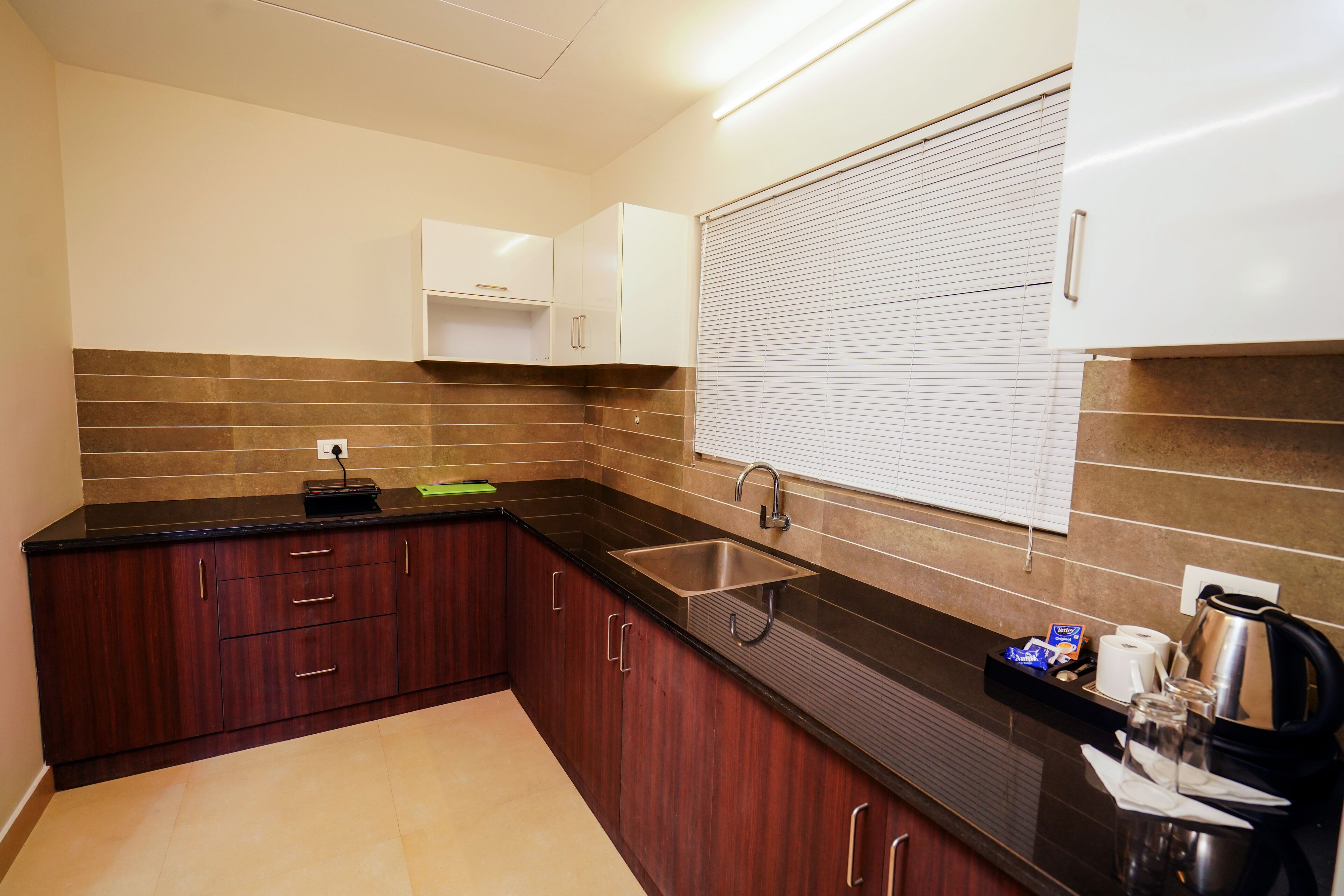 A modern kitchen with dark wooden cabinets, a black countertop, and a stainless steel sink.