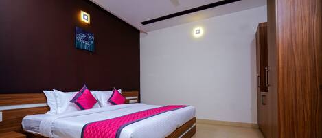 Cama bem arrumada com roupa de cama branca e rosa, cabeceira de madeira e mesa de cabeceira com gaveta.