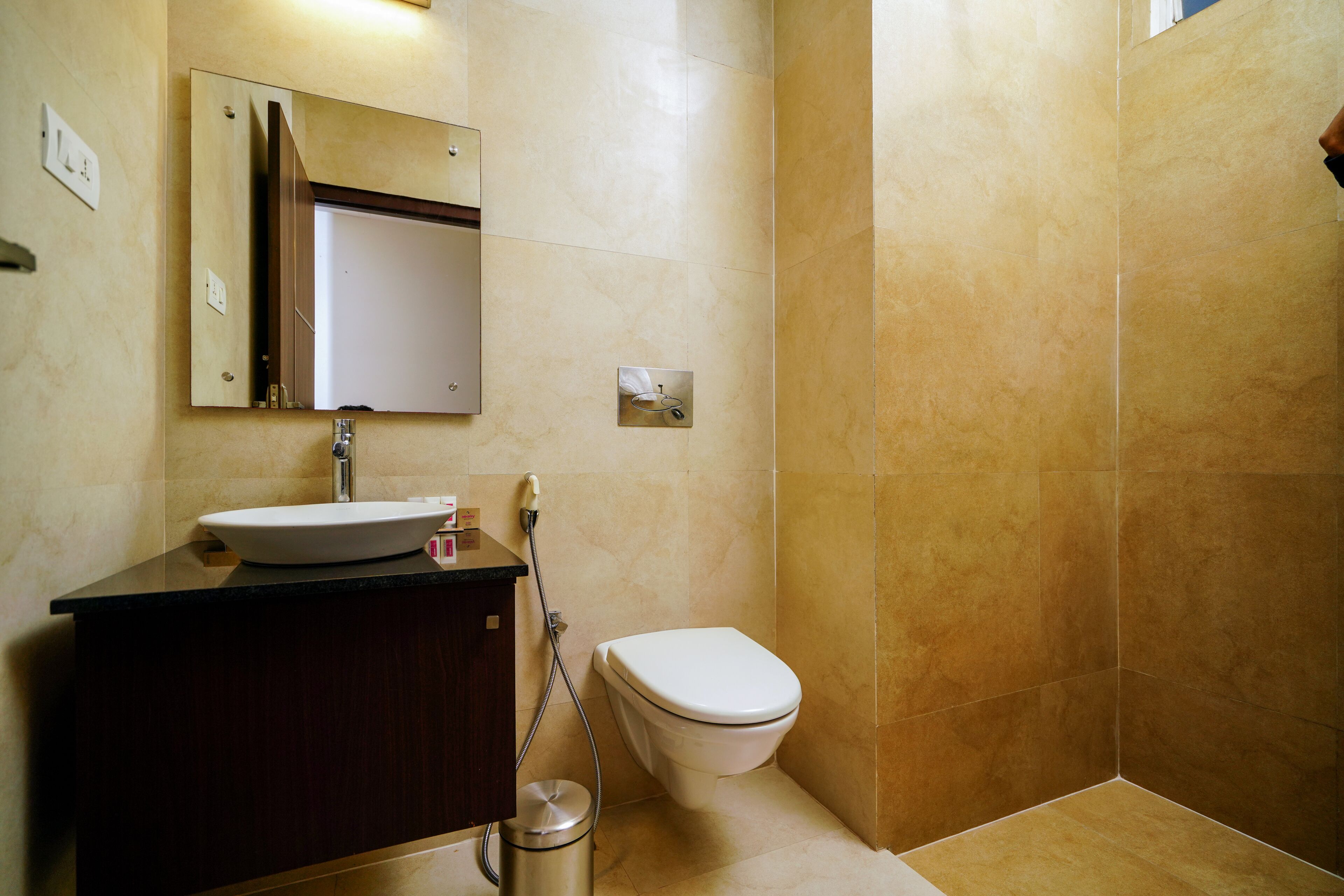 A bathroom with a sink, mirror, toilet, and a trash can.