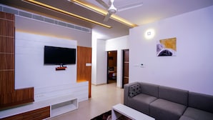 Una sala moderna con televisor de pantalla plana, muebles de madera, un sofá gris y un ventilador de techo.