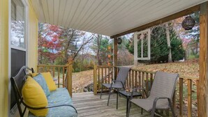 Une véranda couverte avec une terrasse en bois, un banc avec des coussins et deux chaises.