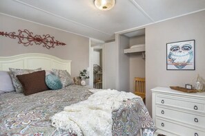 Une chambre à coucher avec une couvre-lit à motifs, une tête de lit blanche et une commode blanche avec des tiroirs.