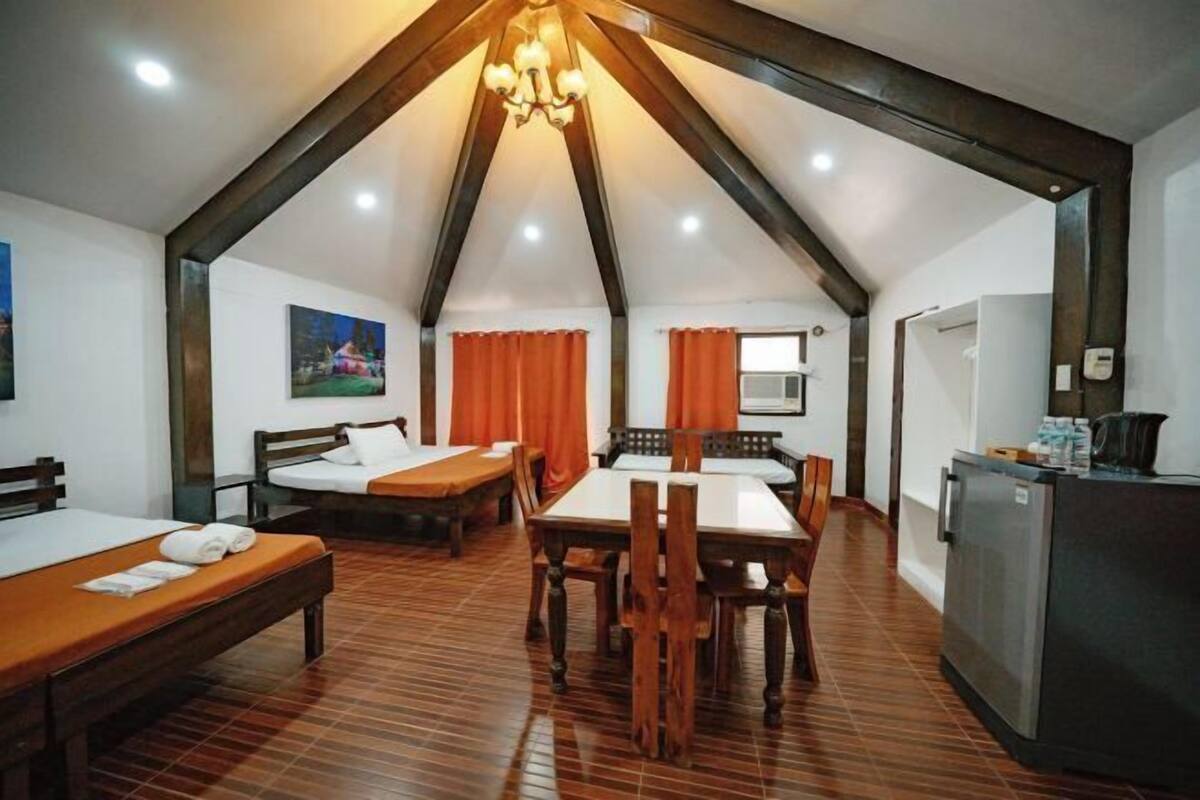 A room with a sloped ceiling, wooden furniture, a dining table, and a kitchenette.