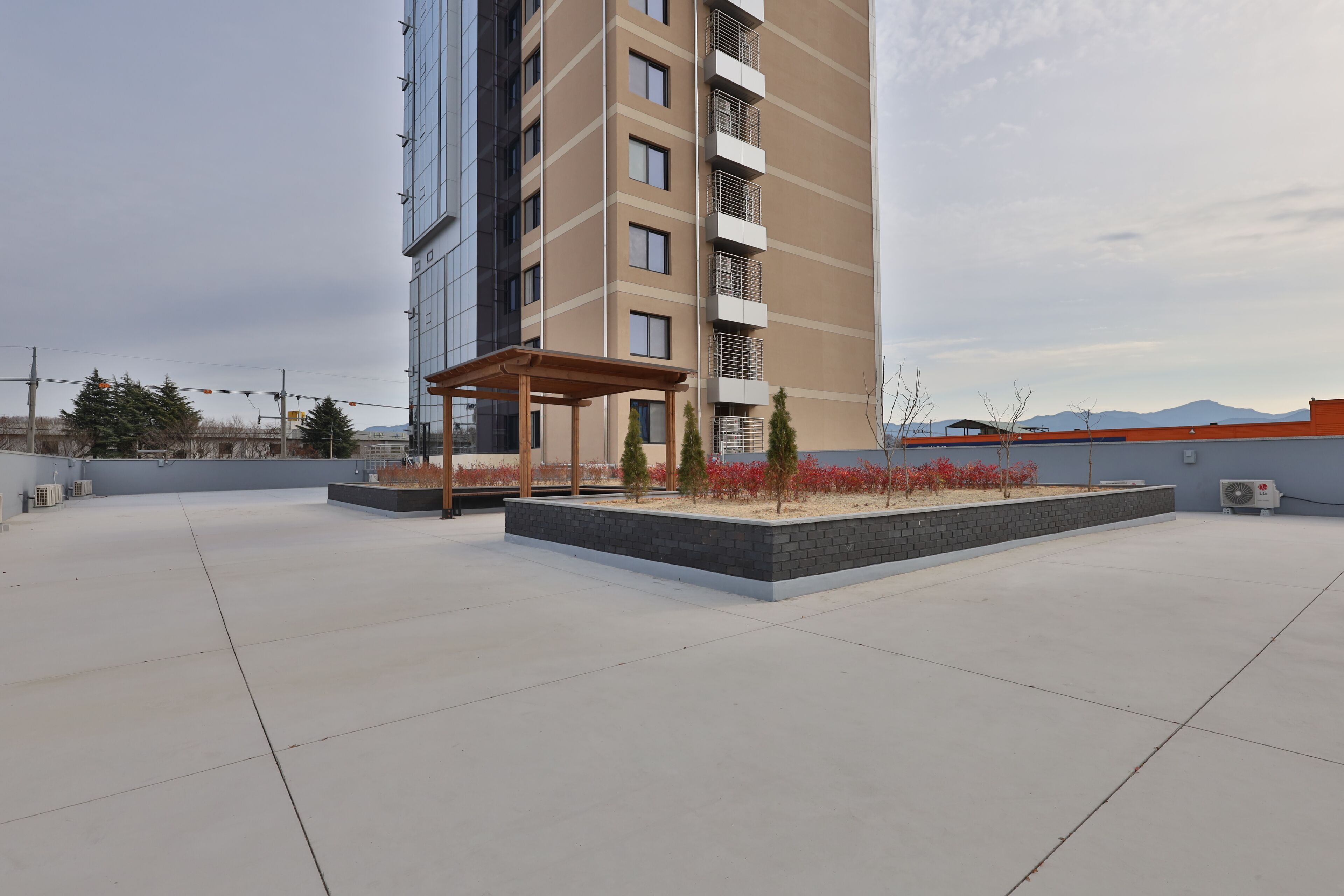A rooftop terrace with a pergola, small trees, and a view of a mountain range.
