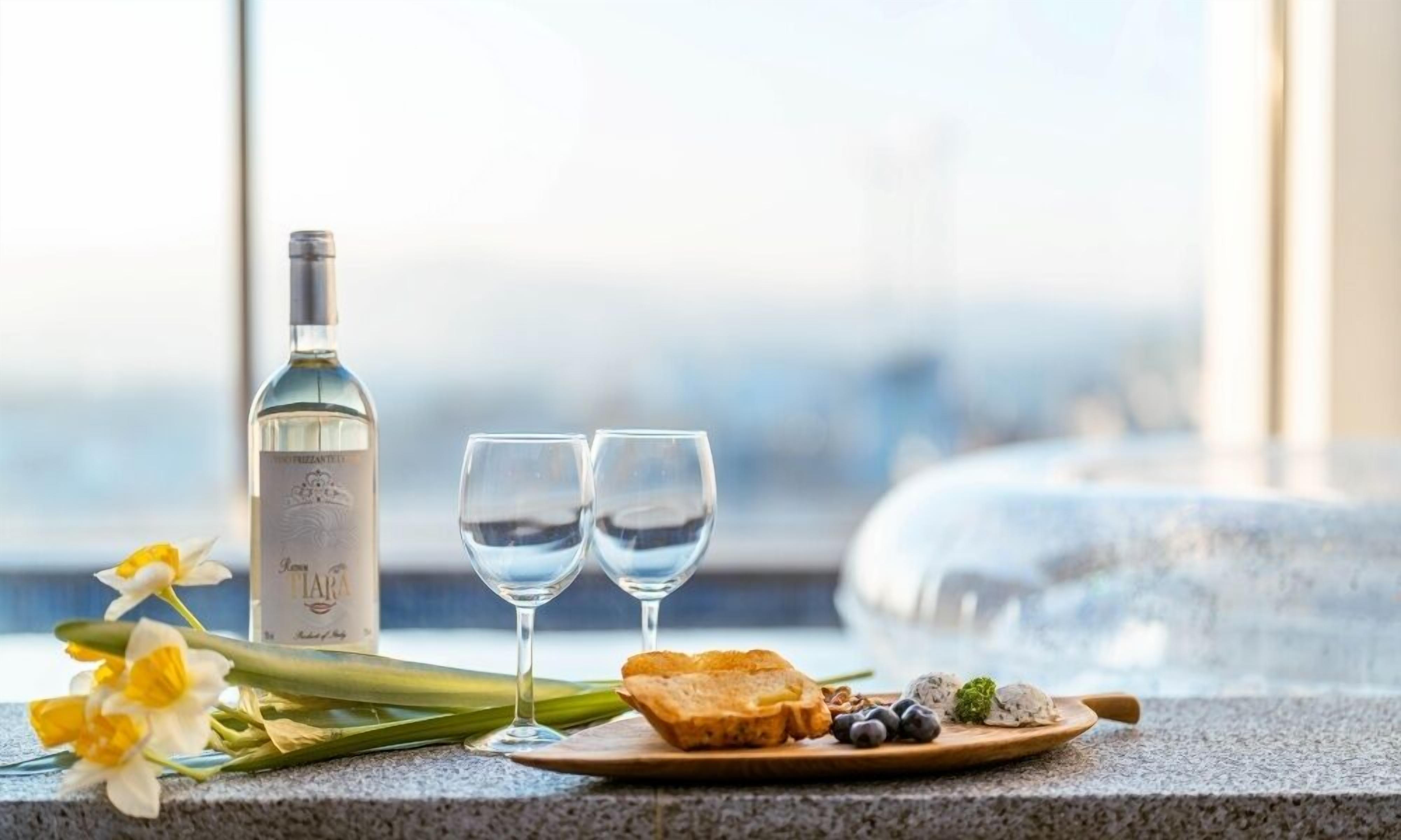 Una botella de vino blanco, dos copas, narcisos y un plato con pan, queso y bayas sobre una encimera de granito.