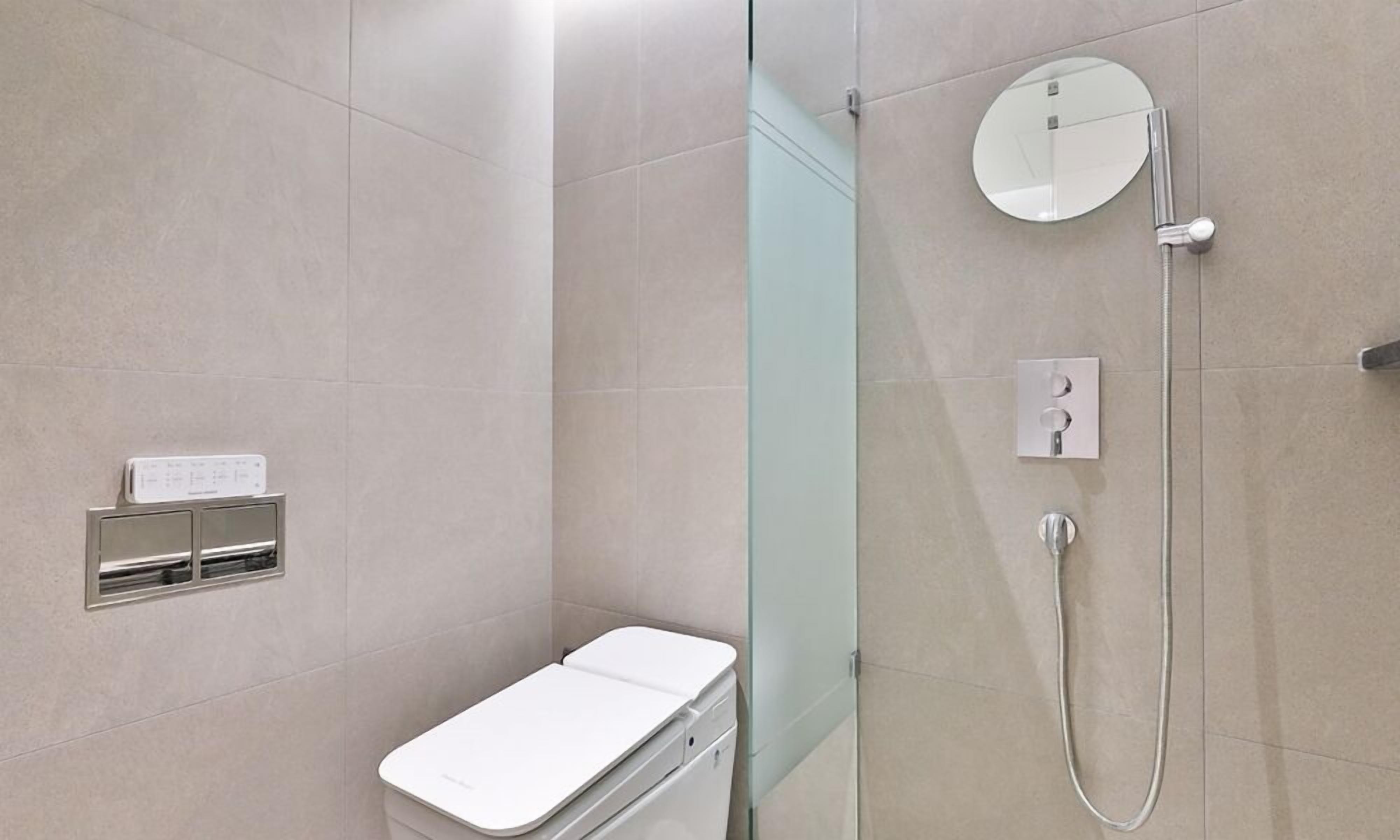 A modern bathroom with a glass shower enclosure, a toilet, and a control panel.
