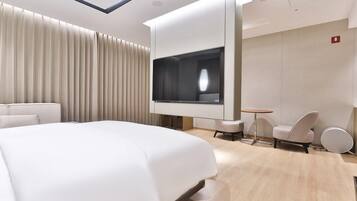 A modern hotel room with a large bed, a TV mounted on the wall, a small round table, and two chairs.