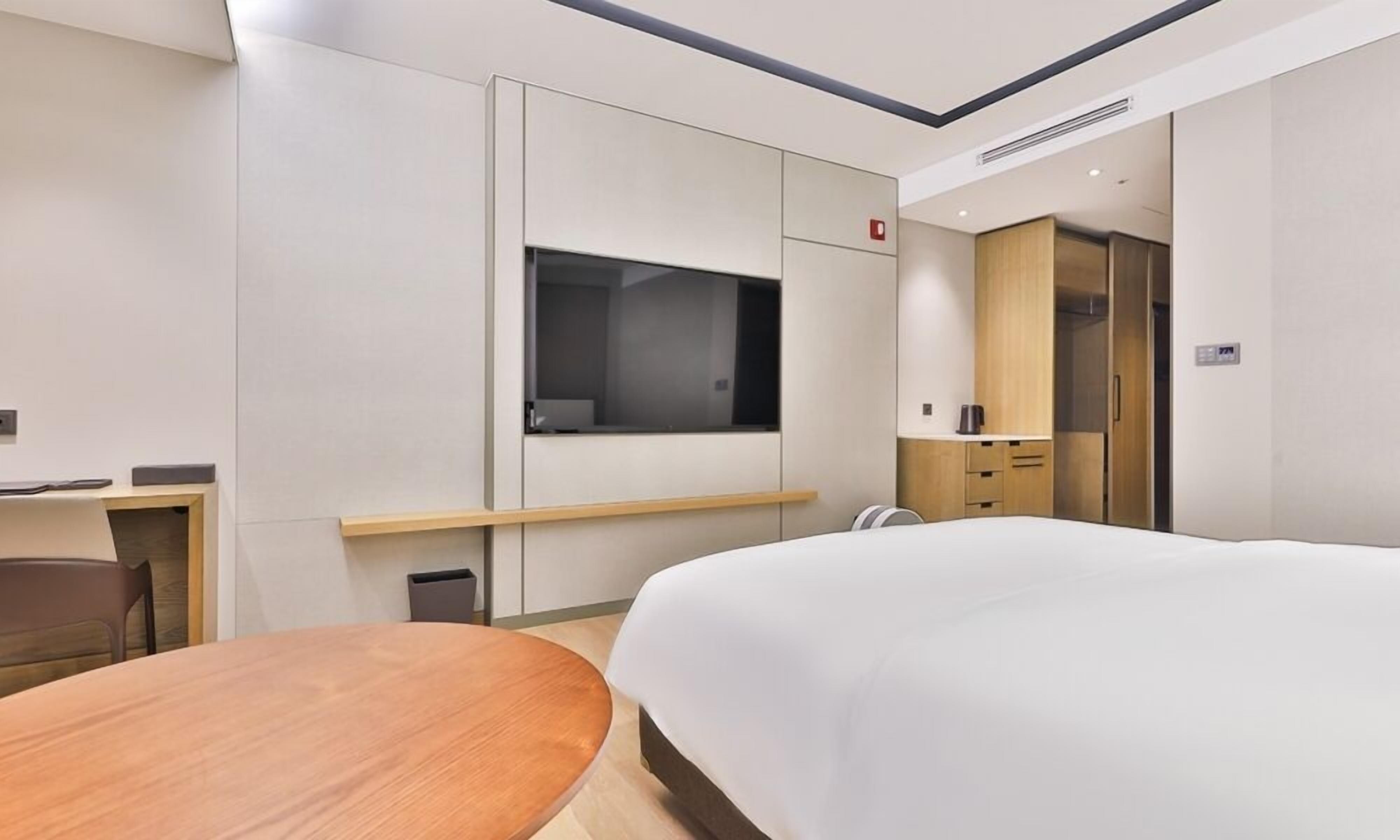 Una habitación de hotel moderna con una cama grande, un escritorio con silla, una mesita, un armario y un espejo.