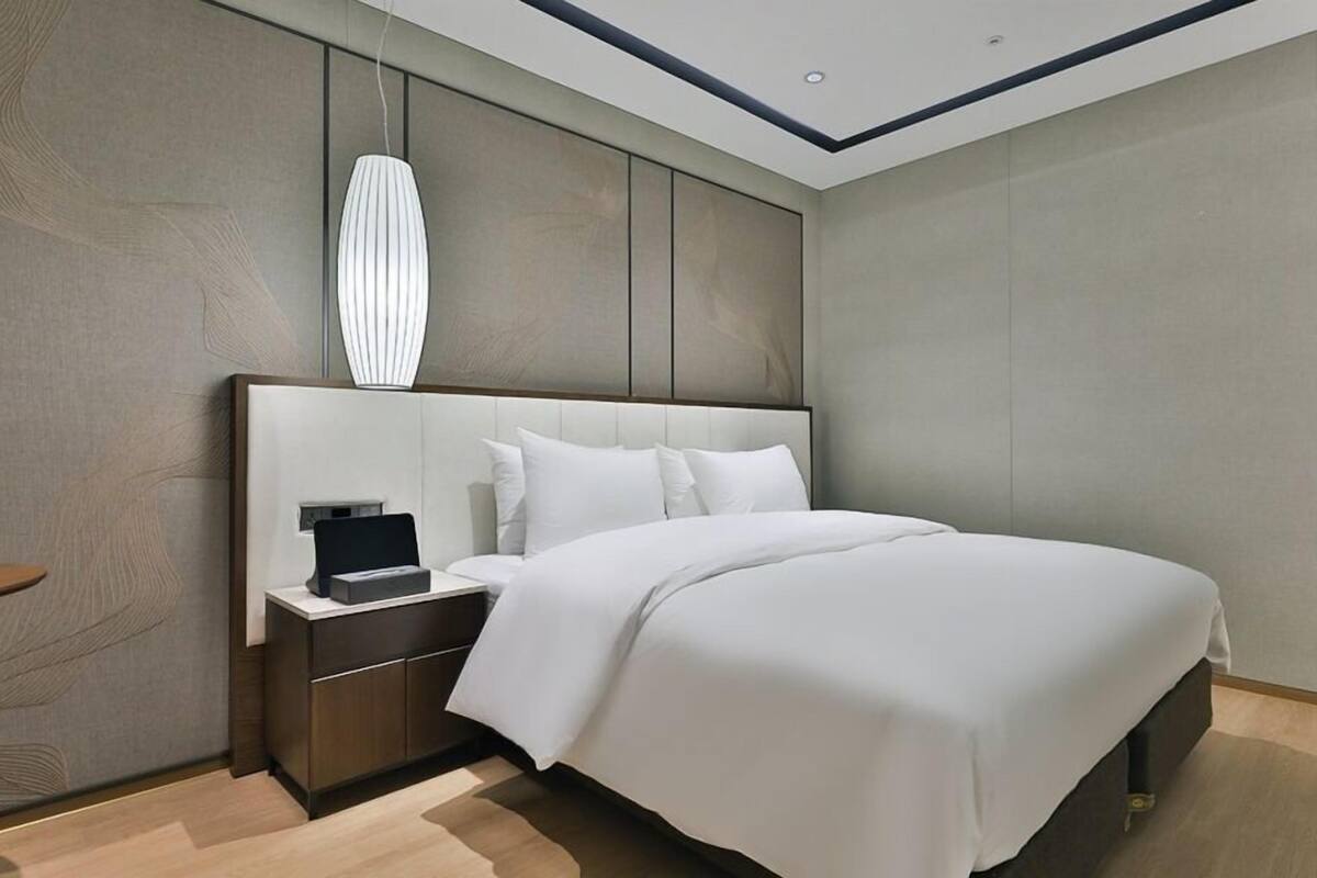 Une chambre moderne avec un grand lit, une table de chevet, une lampe fixée au mur et un plancher en bois.