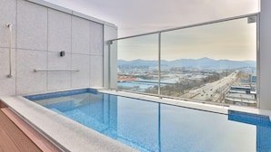 Una piscina interior moderna con vistas a la ciudad, una pared de vidrio y una barandilla de metal.