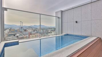 A rooftop pool with a city view, clear sky, and a tiled wall.