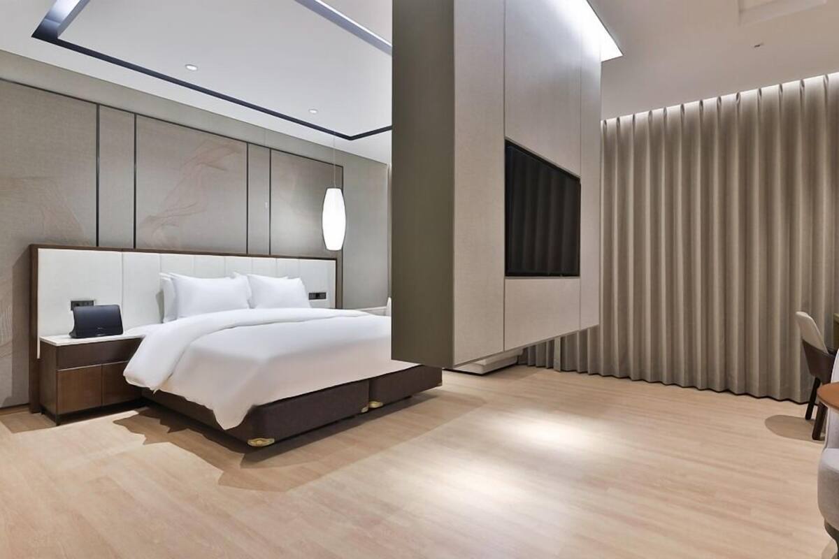 Une chambre d’hôtel moderne avec un grand lit, une table de chevet, une chaise et une fenêtre avec des rideaux.