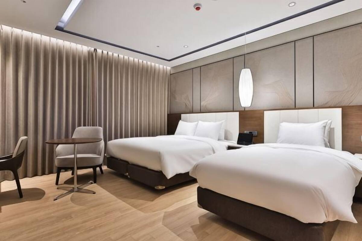 Une chambre d’hôtel avec deux lits, un bureau, une chaise et une grande fenêtre avec des rideaux.