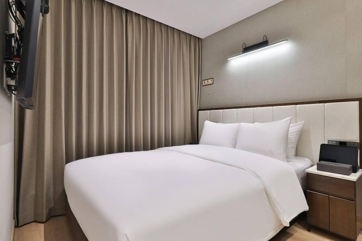 Une chambre d’hôtel avec un grand lit, une table de chevet, un téléviseur à écran plat et un rideau.