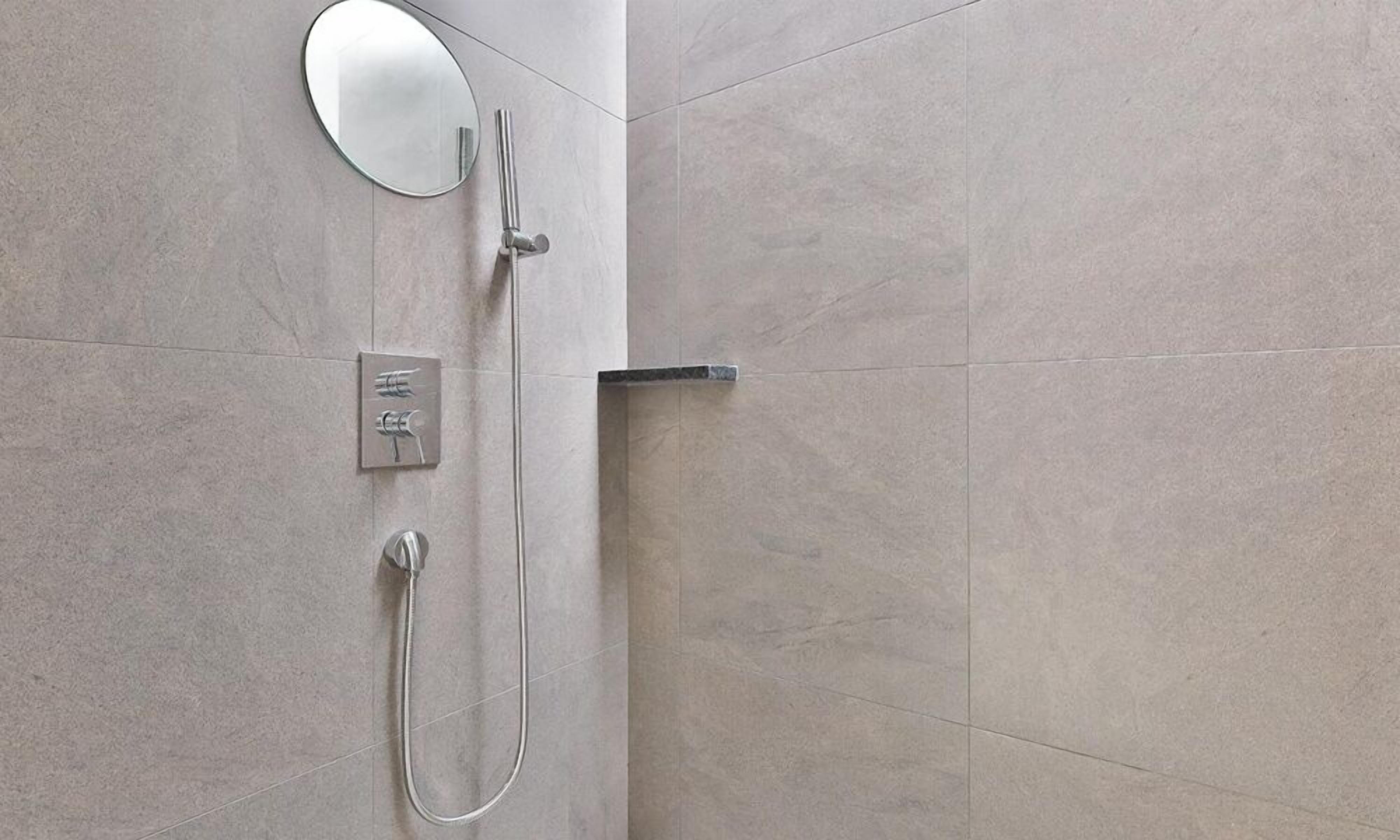 A bathroom with a shower, a mirror, and a control panel.
