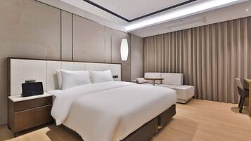 Une chambre d’hôtel moderne dotée d’un grand lit, d’une table de chevet avec une lampe, d’un coin salon avec une petite table et d’une grande fenêtre avec des rideaux.