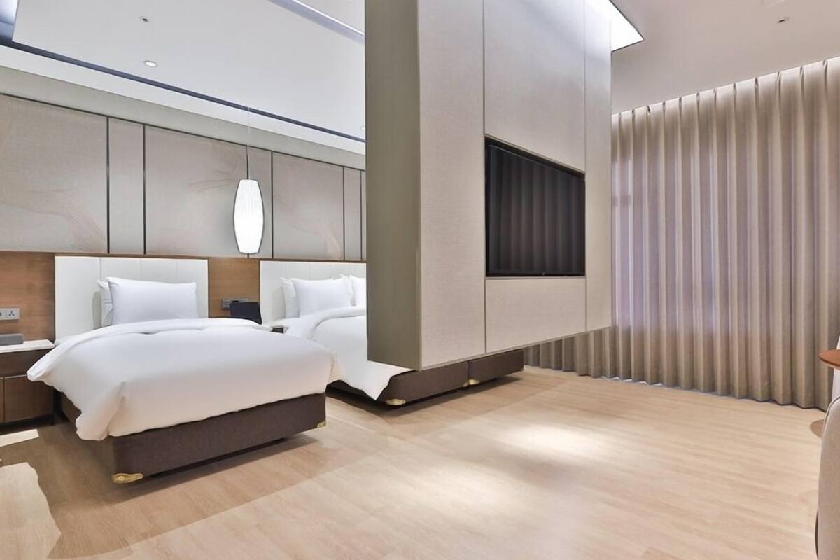 Une chambre d’hôtel moderne avec un grand lit, une table de chevet, une télévision et une fenêtre avec des rideaux.