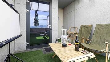 Een balkon met een tafel, stoelen, een projectiescherm en uitzicht op de omgeving.