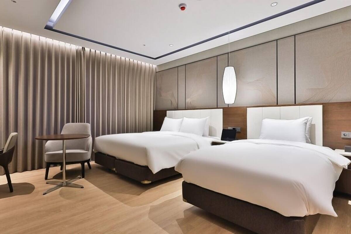 Une chambre d’hôtel moderne équipée de deux lits, d’un bureau, d’une chaise et d’une grande fenêtre avec des rideaux.