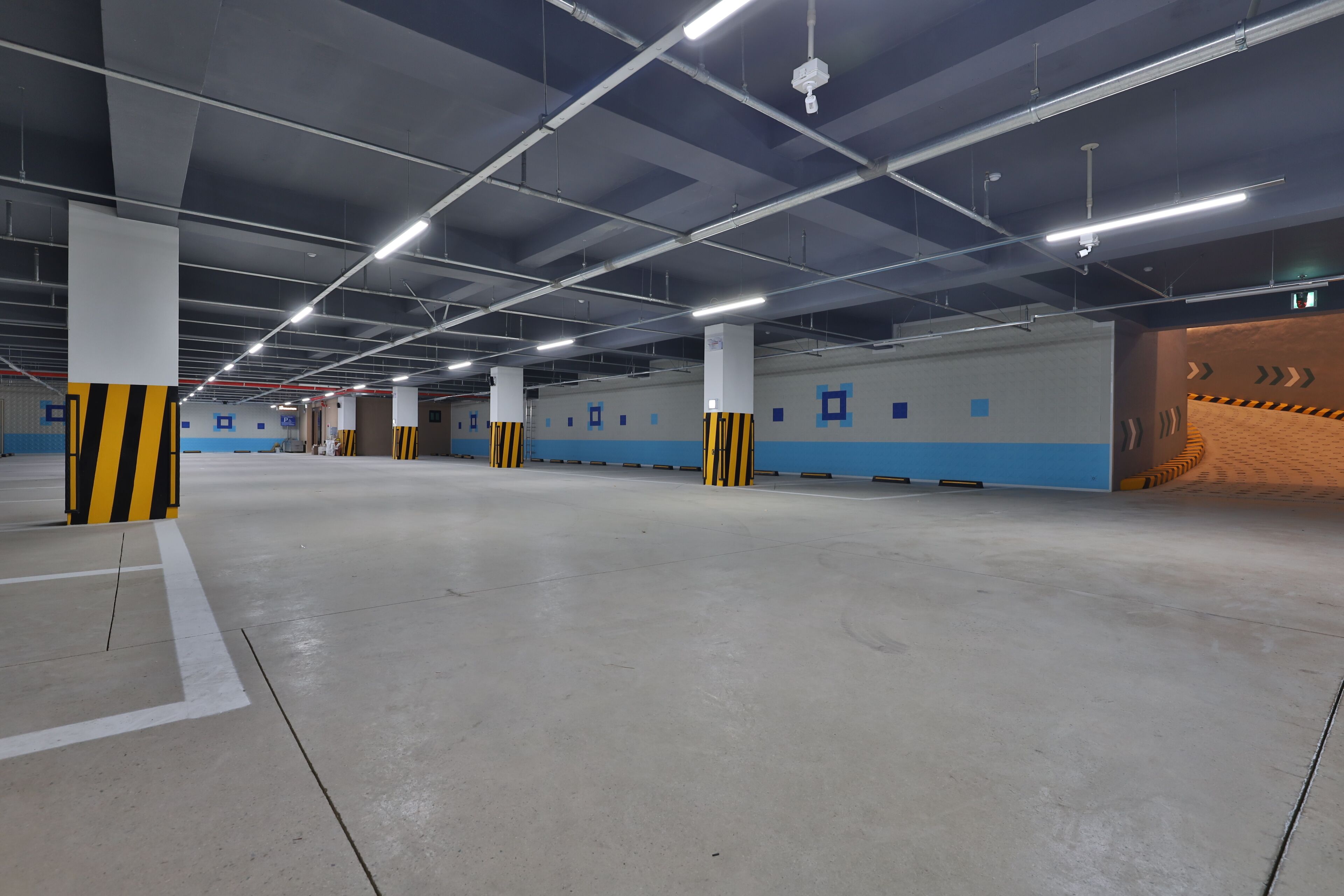 An indoor parking garage with concrete floors, white pillars with yellow stripes, and blue walls with white doorways.