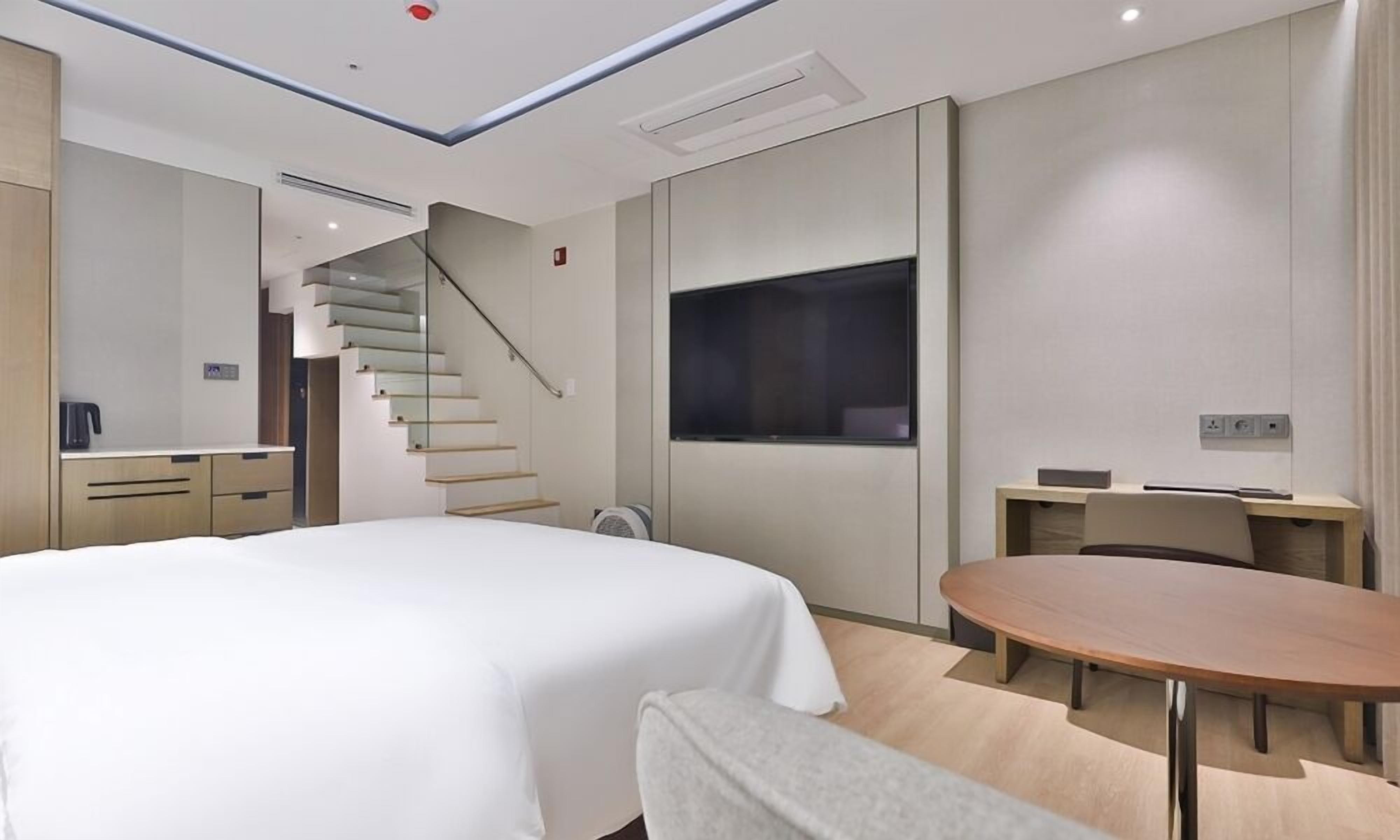 Ein modernes Hotelzimmer mit Bett, Schreibtisch, Stuhl, rundem Tisch, Fernseher und einer Treppe.