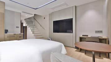 Ein modernes Hotelzimmer mit Bett, Schreibtisch, Stuhl, rundem Tisch, Fernseher und einer Treppe.