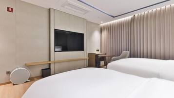 A modern hotel room with two beds, a desk, a chair, and a large window with curtains.